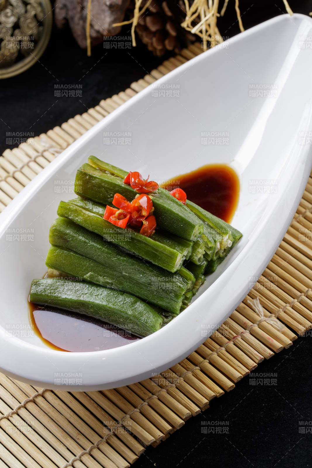 寿司帘上的元宝形瓷盘装的浇汁秋葵-摄影图