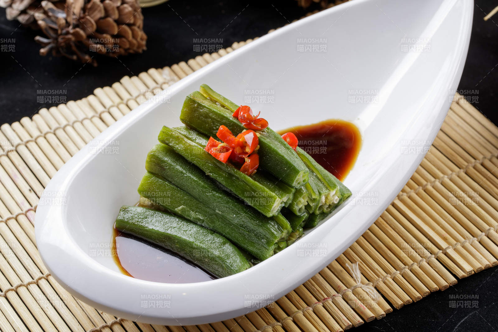寿司帘上的元宝形瓷盘装的浇汁秋葵-摄影图