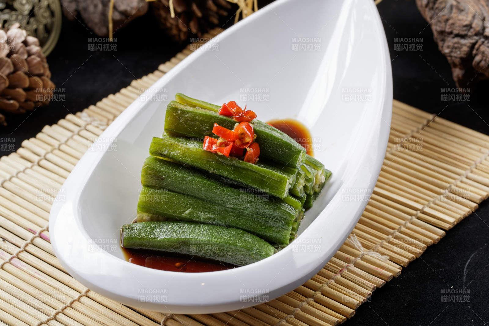 寿司帘上的元宝形瓷盘装的浇汁秋葵-摄影图