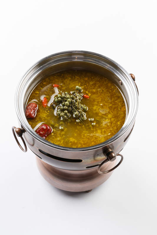 白色背景上的小火锅装的牛油藤椒酸辣锅底