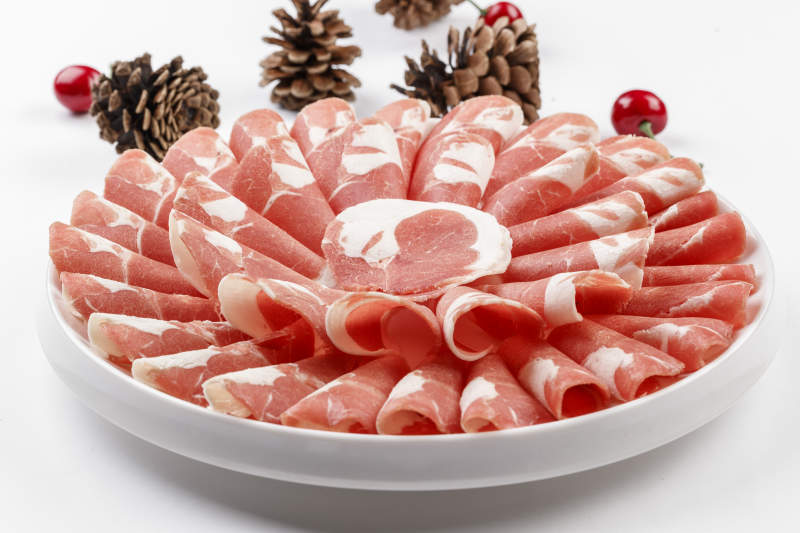 白色背景上的圓瓷盤裝的涮鍋食材肥牛片