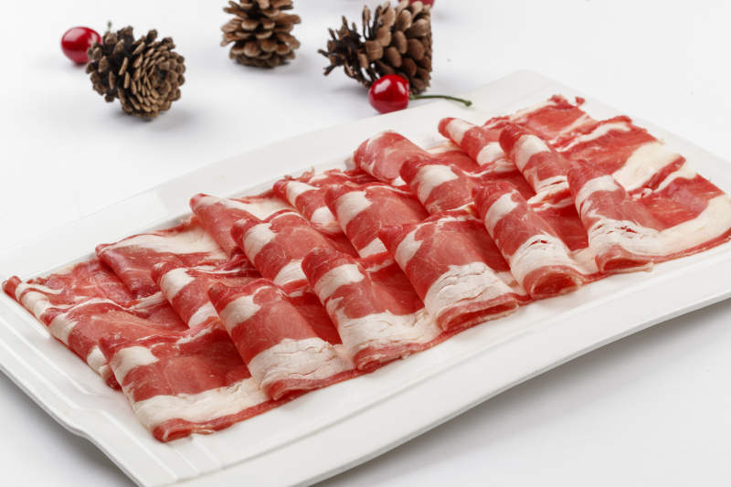 白色背景上的長瓷盤裝的涮肉食材羊肉片