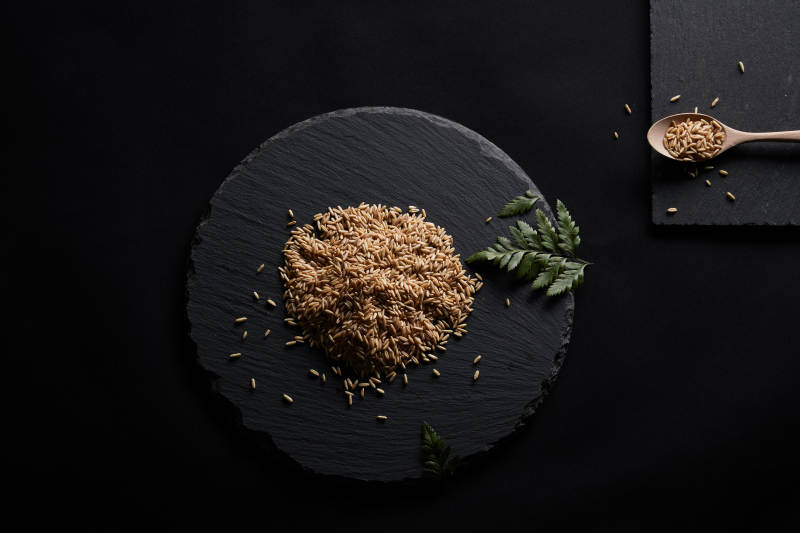 黑色青石板上的木质勺子装的燕麦米摆放在黑色背景中