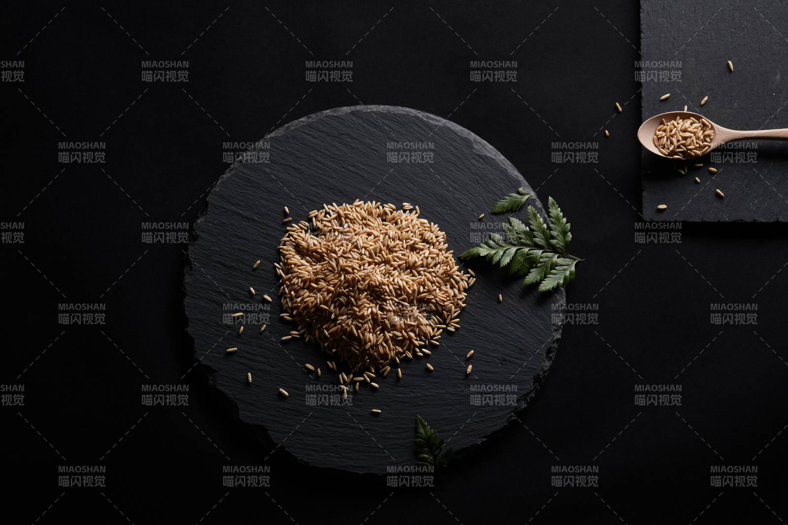 黑色青石板上的木质勺子装的燕麦米摆放在黑色背景中