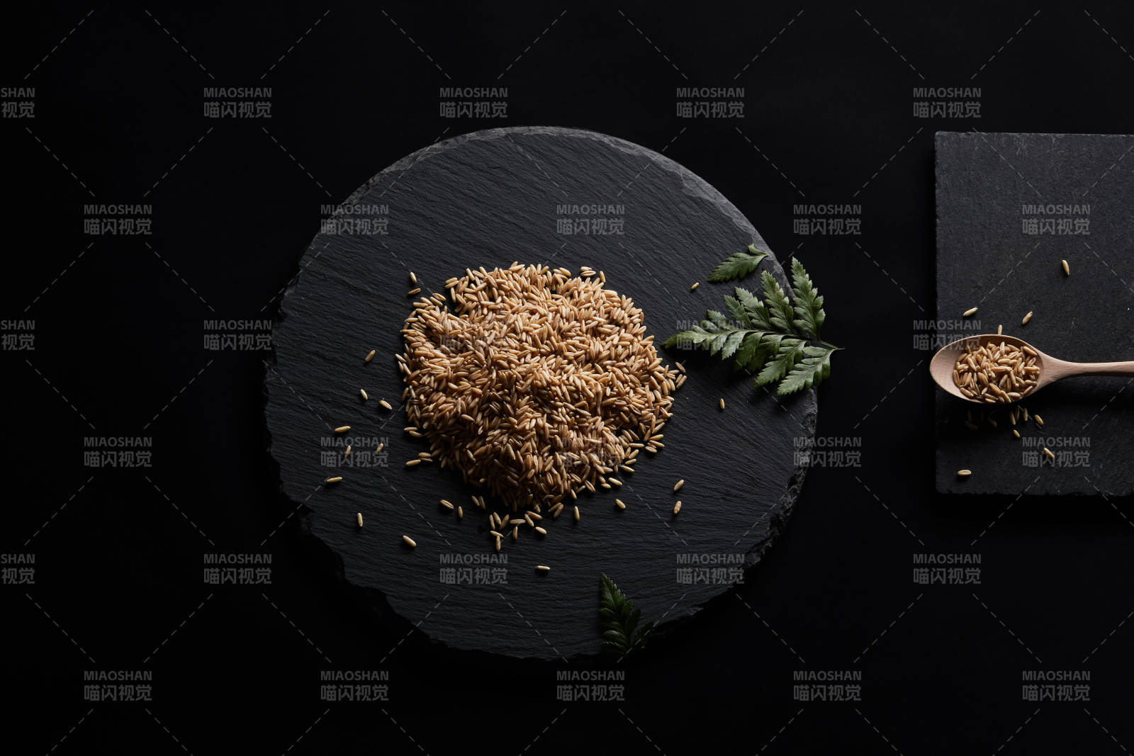 黑色青石板上的木质勺子装的燕麦米摆放在黑色背景中