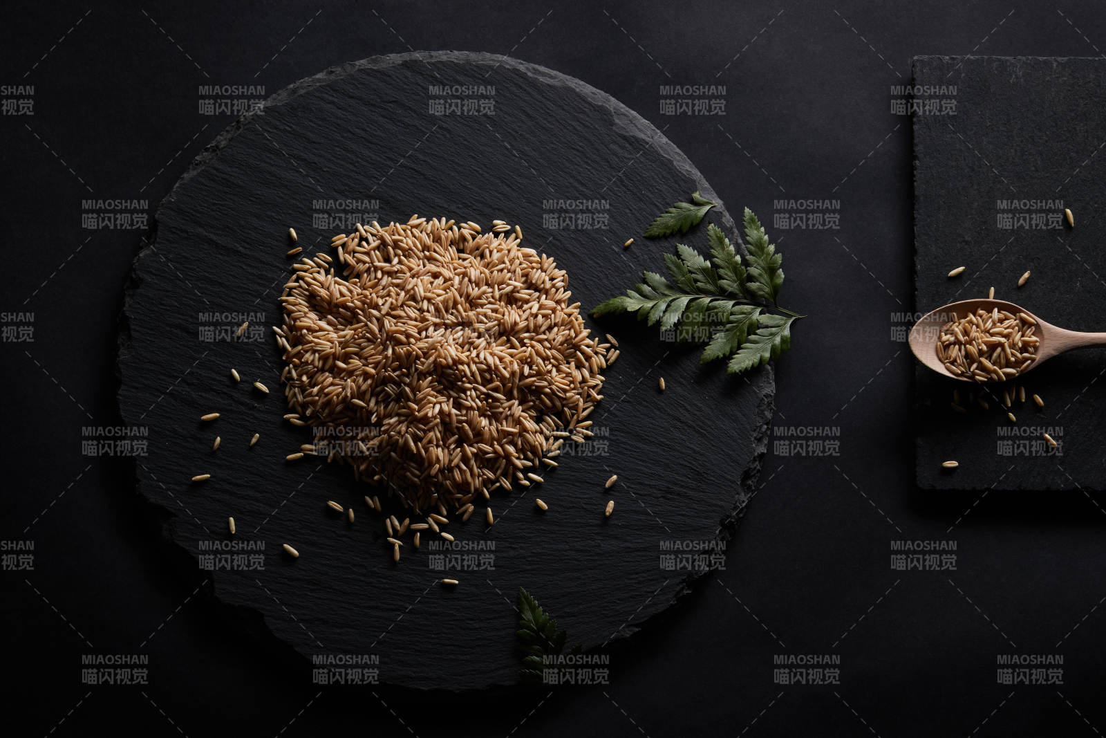 黑色青石板上的木质勺子装的燕麦米摆放在黑色背景中