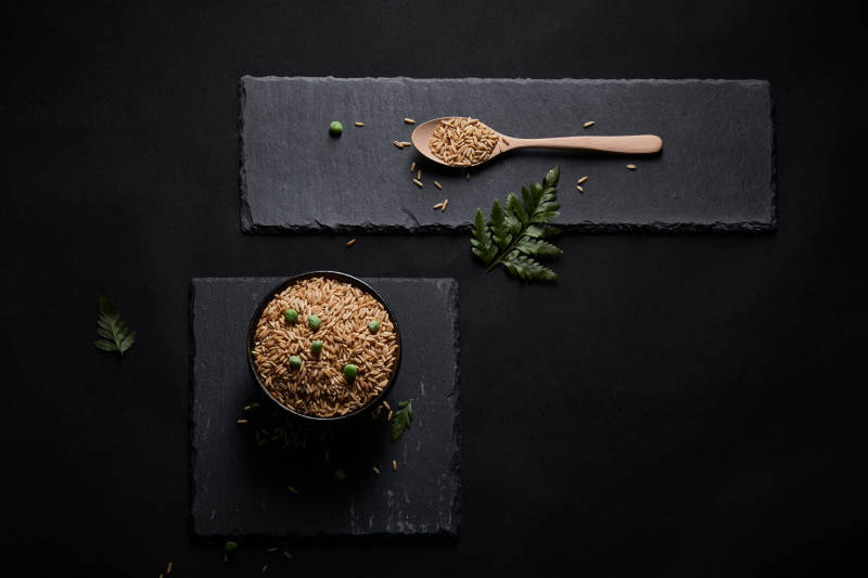 黑色青石板上的木质勺子装的燕麦米摆放在黑色背景中