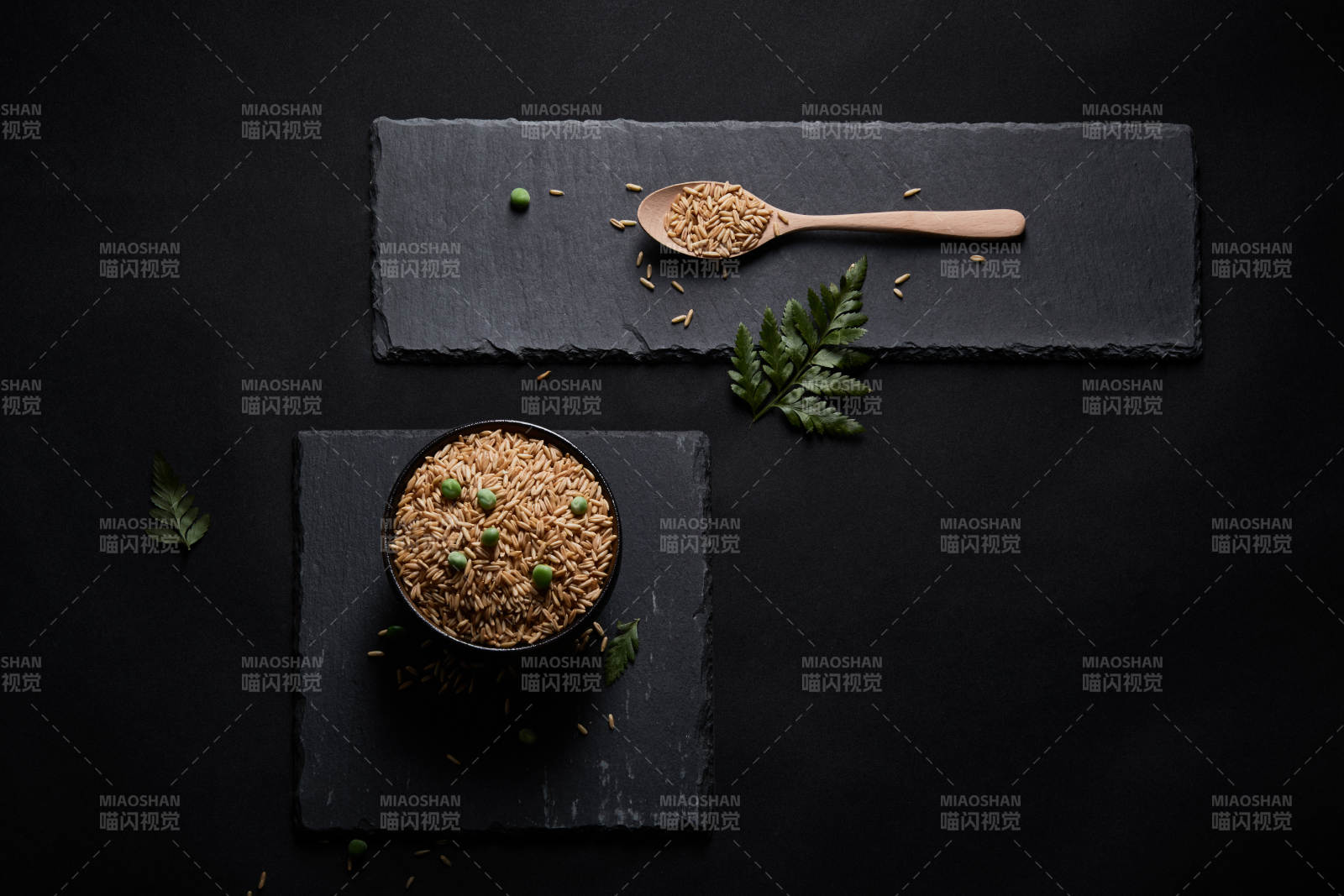 黑色青石板上的木质勺子装的燕麦米摆放在黑色背景中