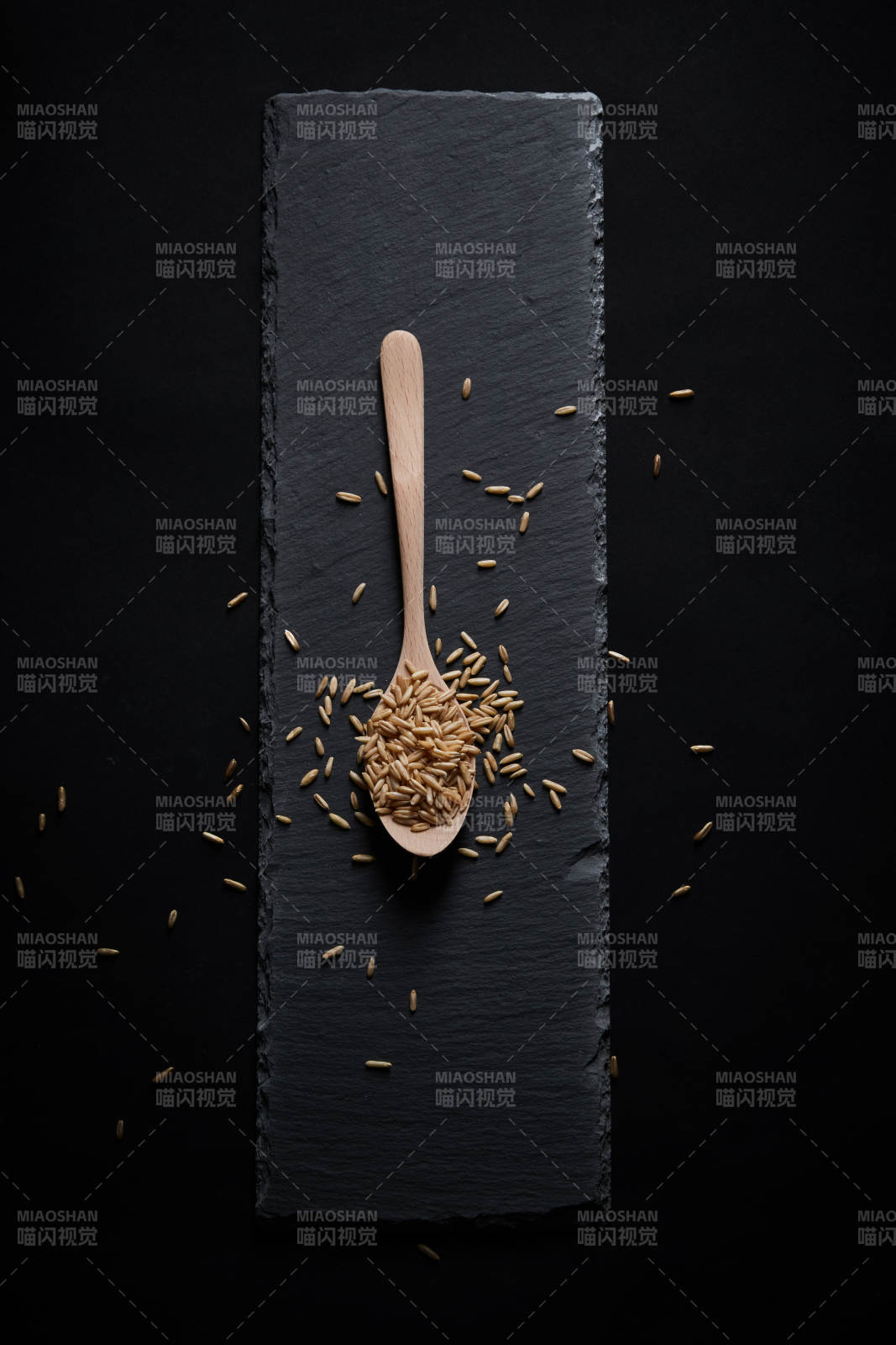 黑色青石板上的木質勺子裝的燕麥米擺放在黑色背景中