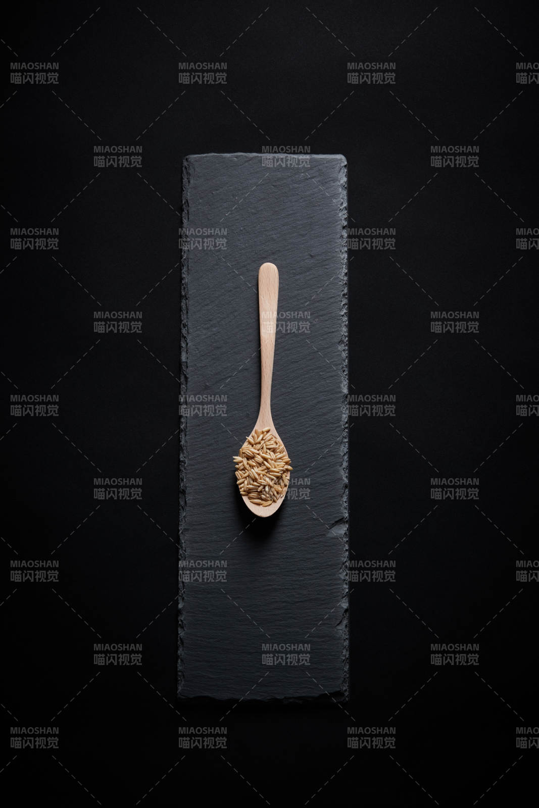 黑色青石板上的木质勺子装的燕麦米摆放在黑色背景中