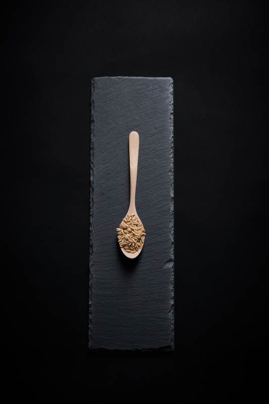 黑色青石板上的木质勺子装的燕麦米摆放在黑色背景中