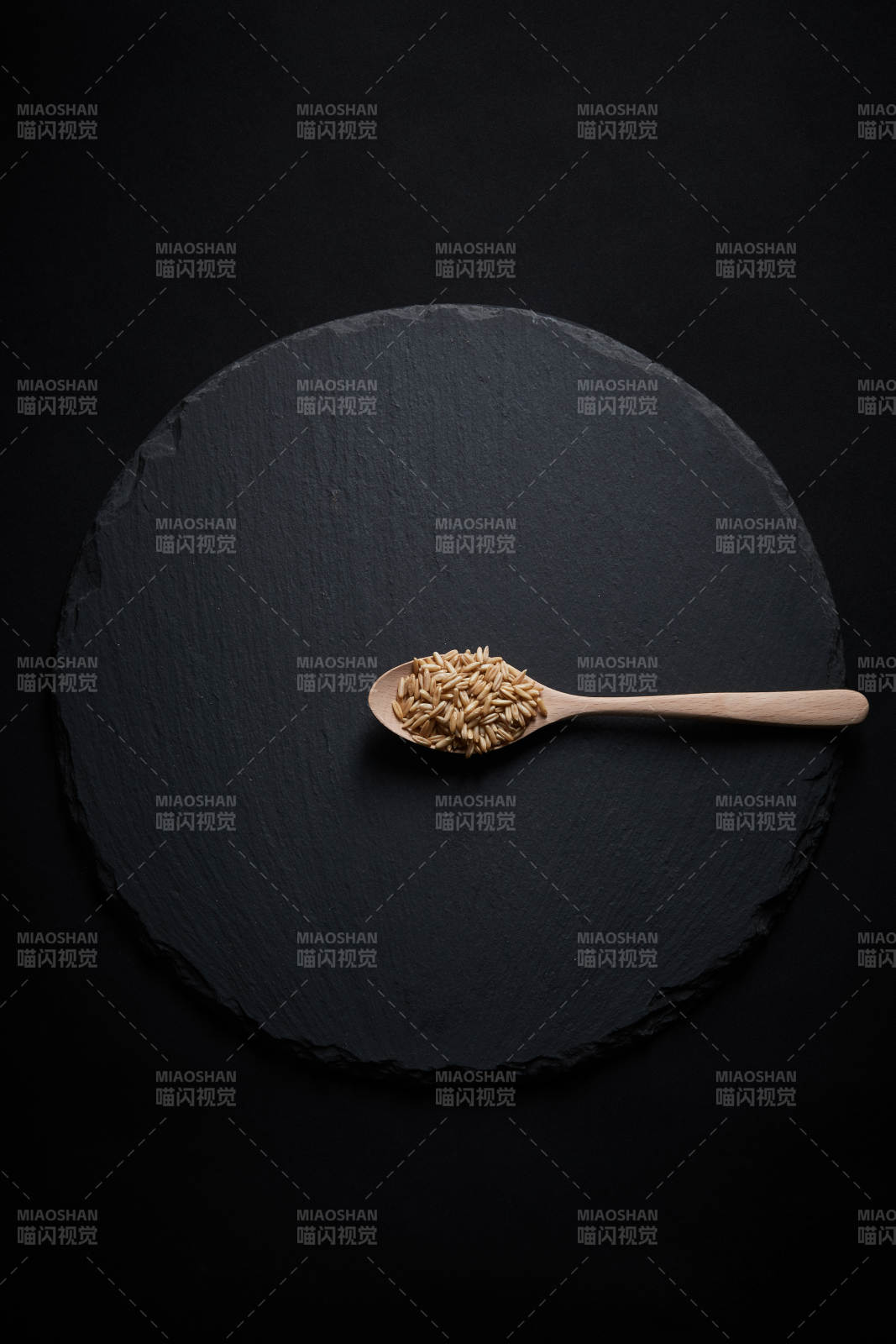 黑色青石板上的木质勺子装的燕麦米摆放在黑色背景中