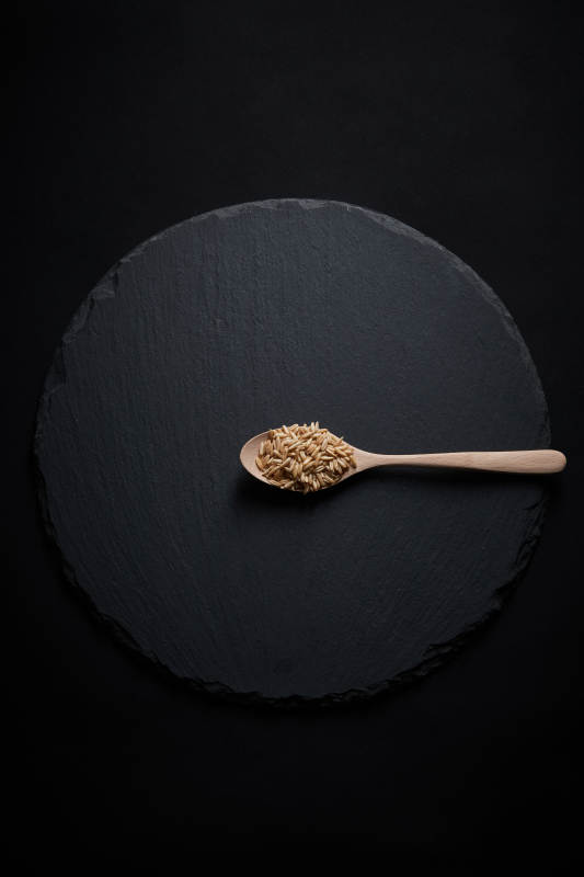 黑色青石板上的木质勺子装的燕麦米摆放在黑色背景中