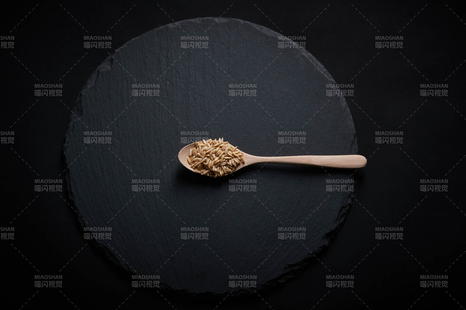 黑色青石板上的木质勺子装的燕麦米摆放在黑色背景中