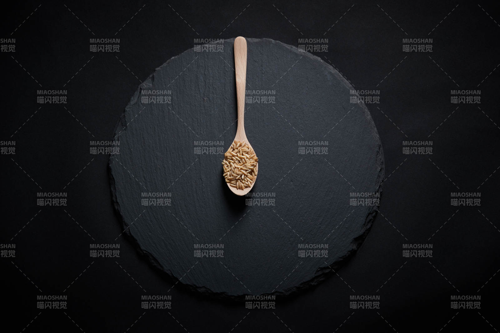 黑色青石板上的木质勺子装的燕麦米摆放在黑色背景中