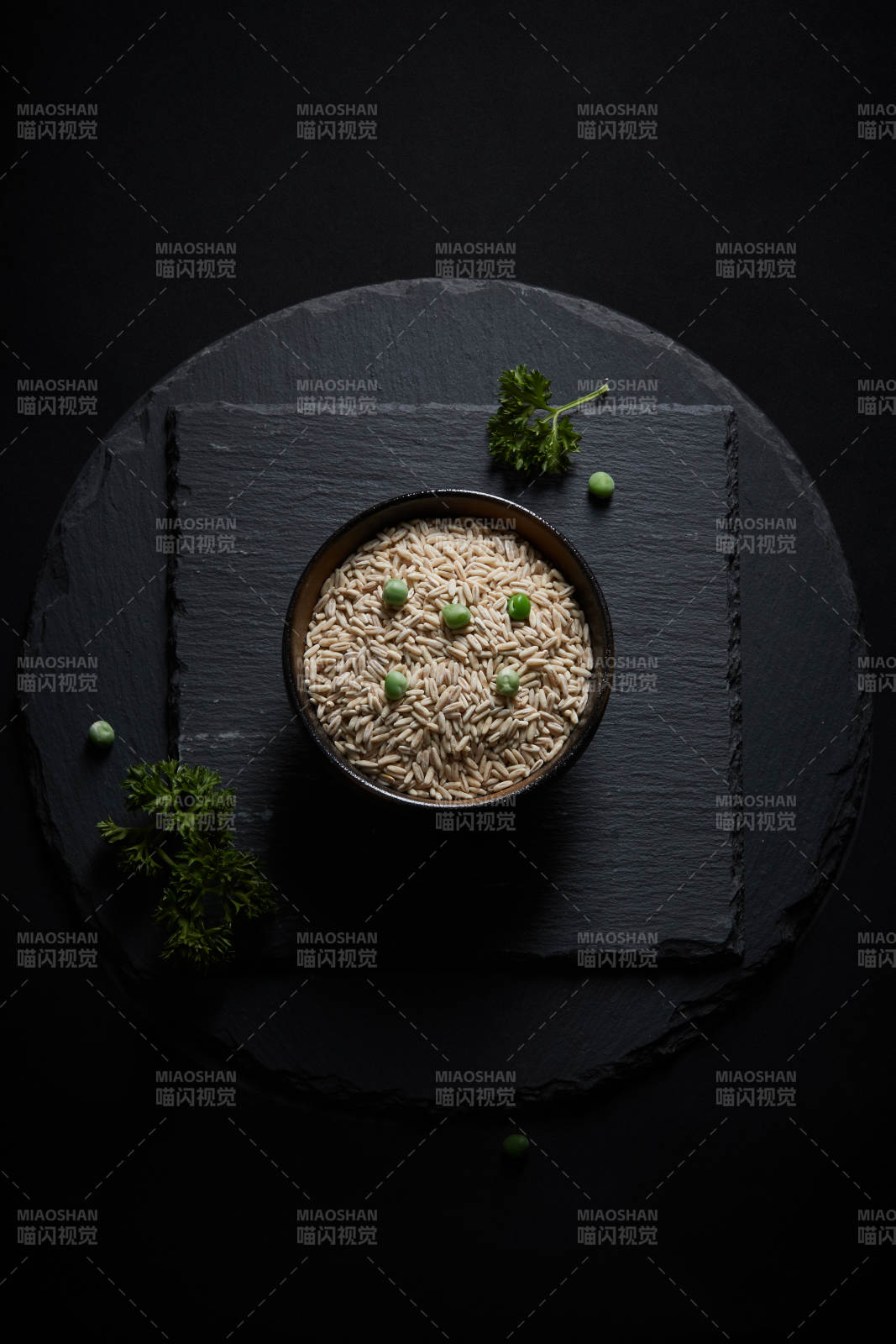 黑色青石板上的木质勺子装的燕麦米摆放在黑色背景中