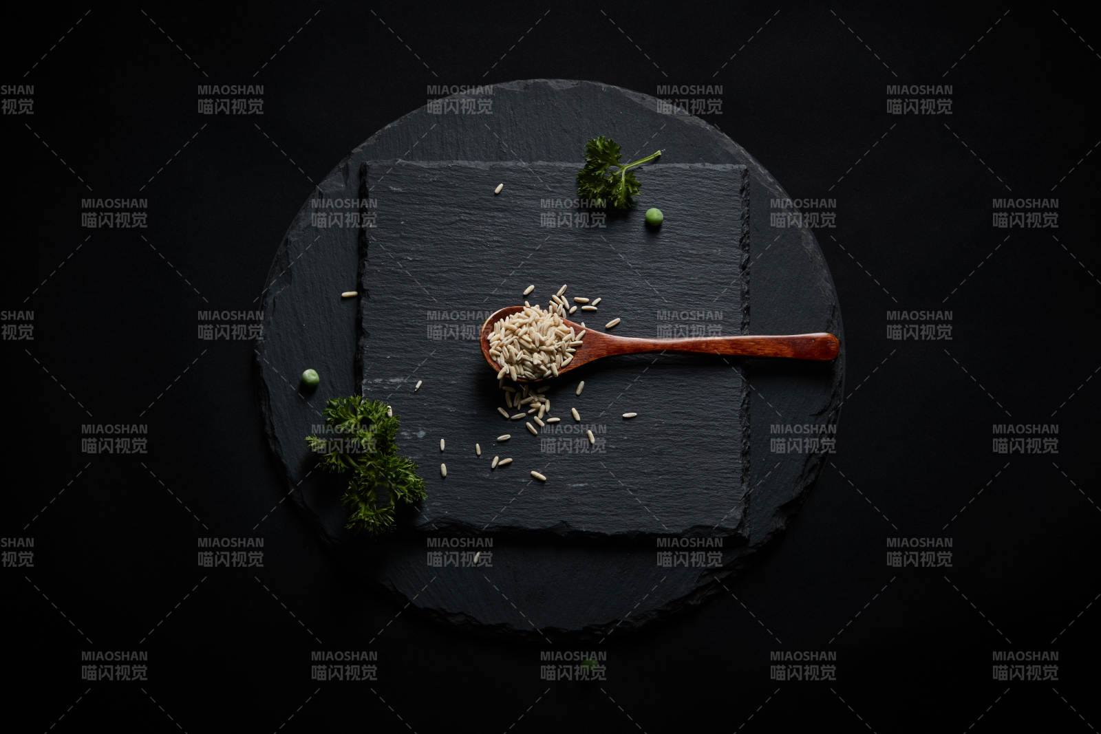 黑色青石板上的木质勺子装的燕麦米摆放在黑色背景中
