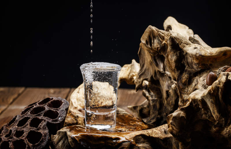 向木板上摆放的酒具内倒入清澈的白酒激起无数酒花