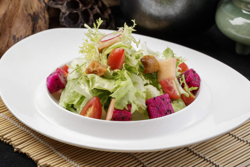 托圆瓷盘装的果蔬拌菜摆放在寿司帘上