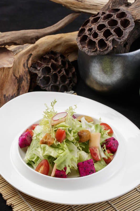 托圆瓷盘装的果蔬拌菜摆放在寿司帘上