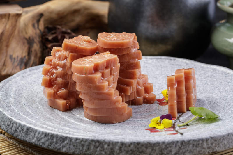 灰色螺旋瓷盘装的蜂蜜黄米藕摆放在寿司帘上