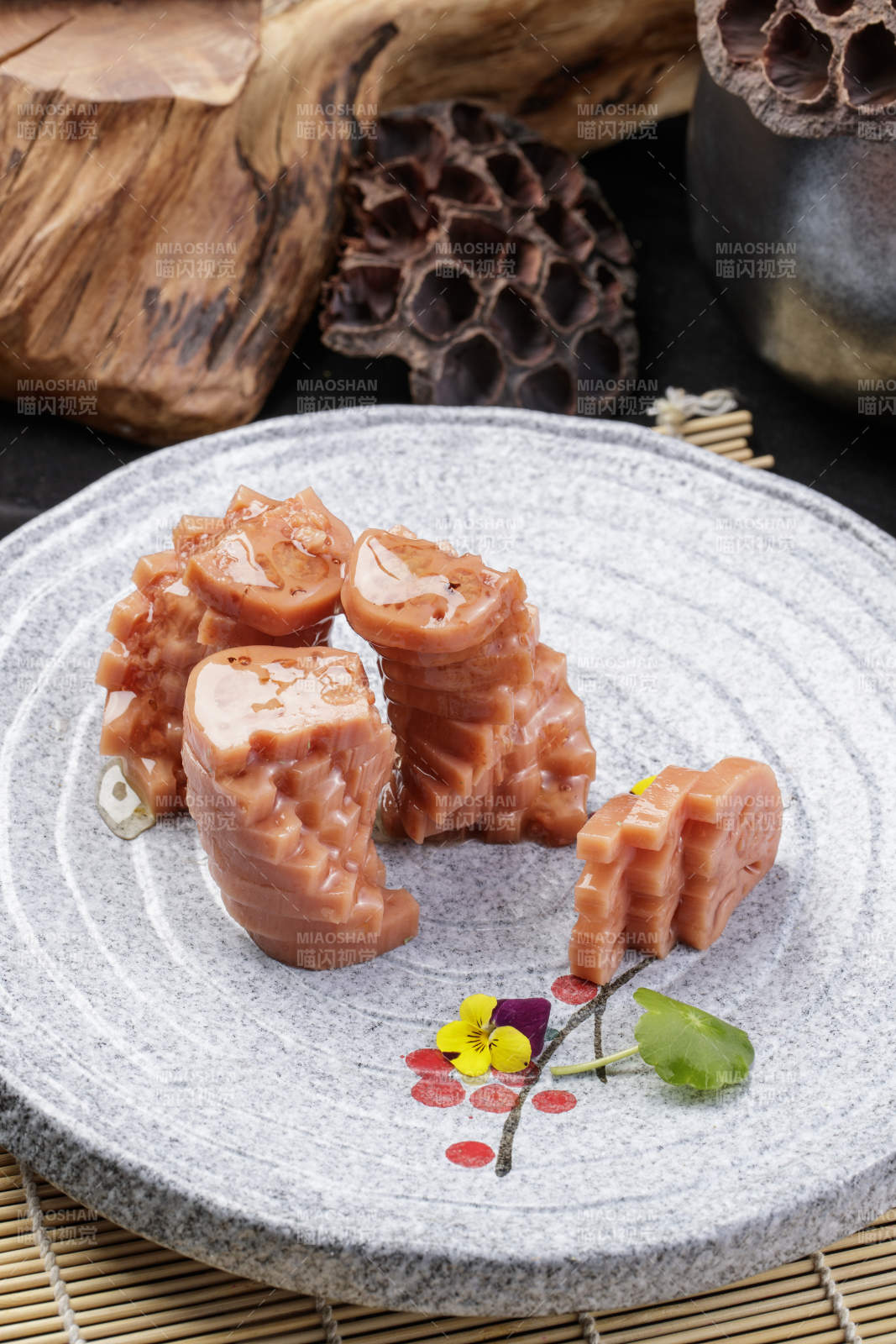 灰色螺旋瓷盘装的蜂蜜黄米藕摆放在寿司帘上