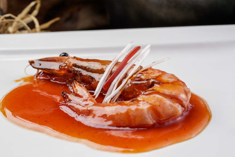 方形瓷盤裝的澆汁大明蝦擺放在樟木砧板上