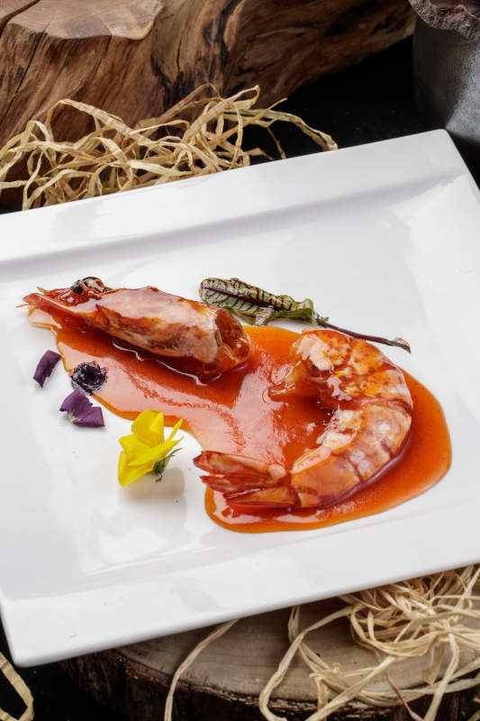 方形瓷盤裝的澆汁大明蝦擺放在樟木砧板上