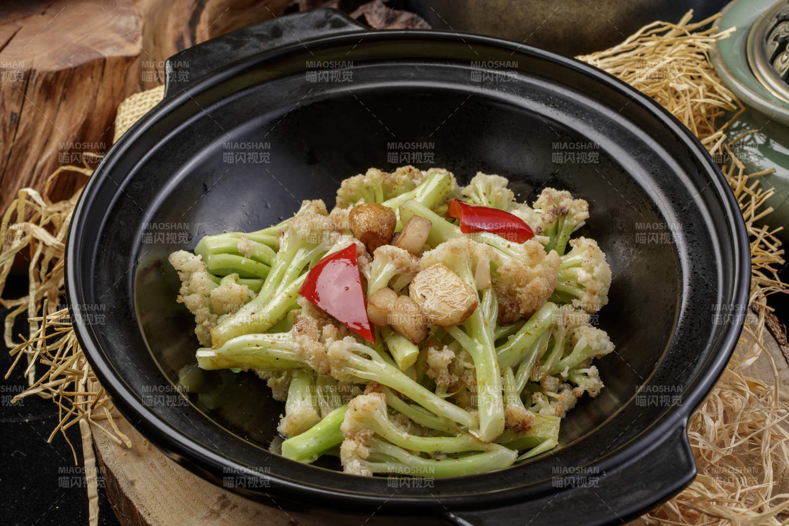 黑色砂锅装的蒜香有机菜花摆放在樟木砧板上