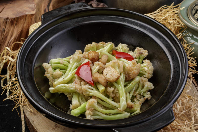 黑色砂锅装的蒜香有机菜花摆放在樟木砧板上