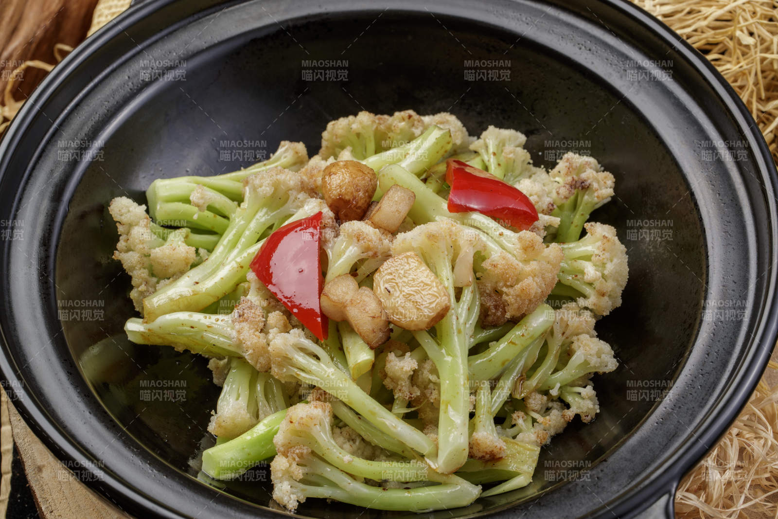 黑色砂锅装的蒜香有机菜花摆放在樟木砧板上