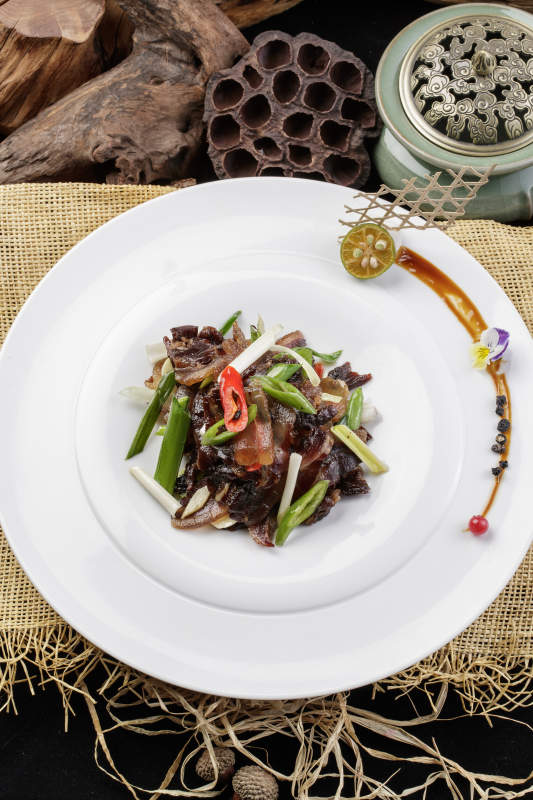 圆形瓷盘装的杭椒蒜薹炒黑腊肉摆放在麻布垫子上