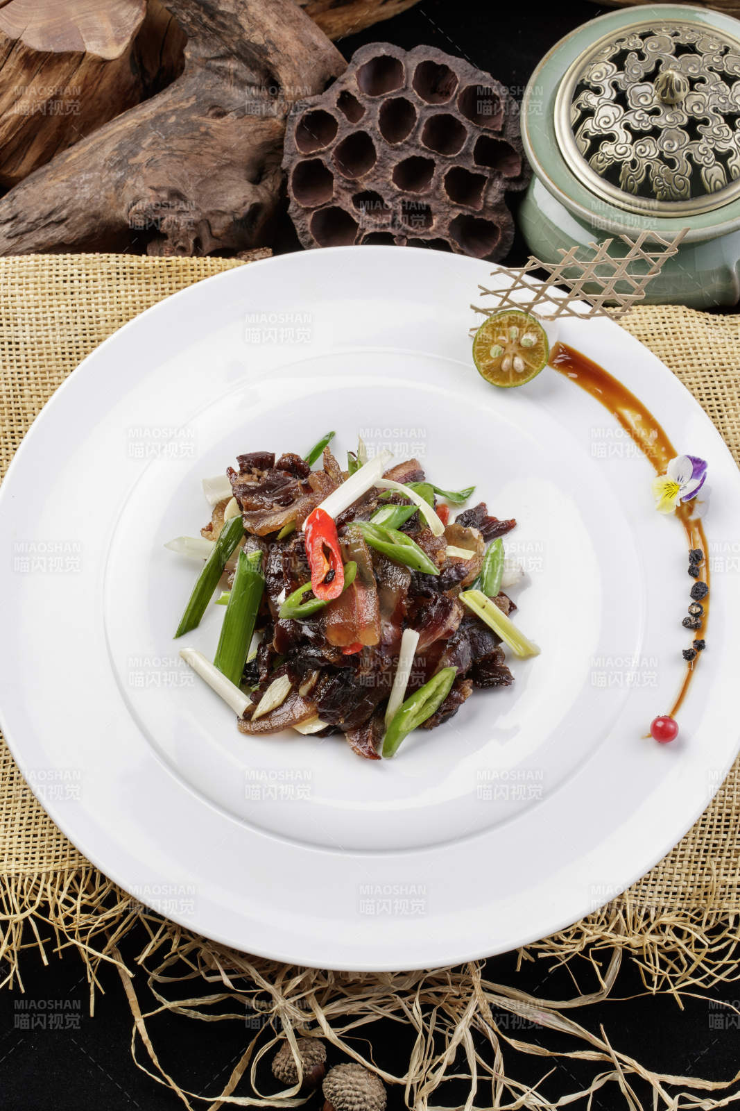 圆形瓷盘装的杭椒蒜薹炒黑腊肉摆放在麻布垫子上