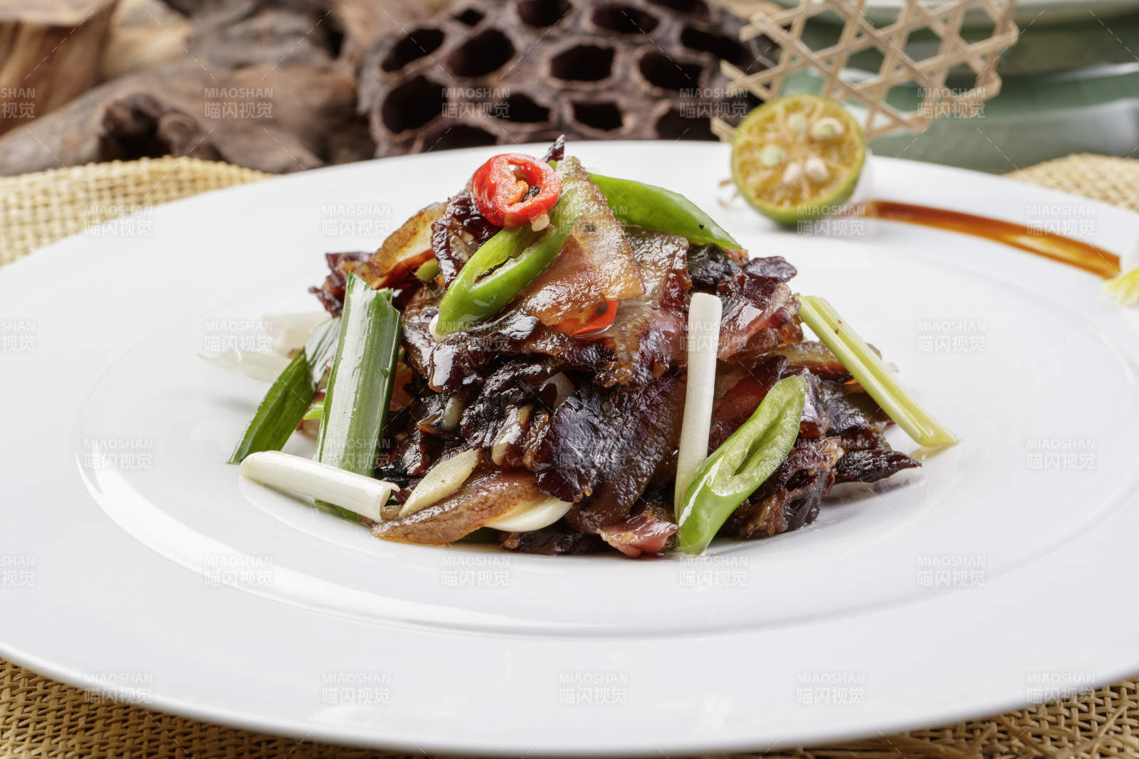 圆形瓷盘装的杭椒蒜薹炒黑腊肉摆放在麻布垫子上