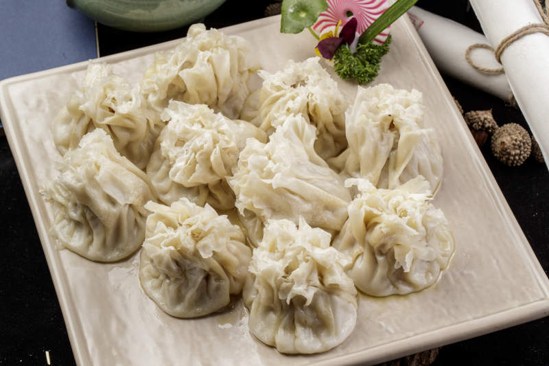 米色瓷盘装的美味烧麦摆放在黑色背景上