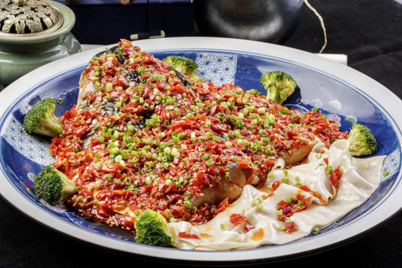 青花瓷盘装的剁椒鱼头盖面摆放在黑色背景上