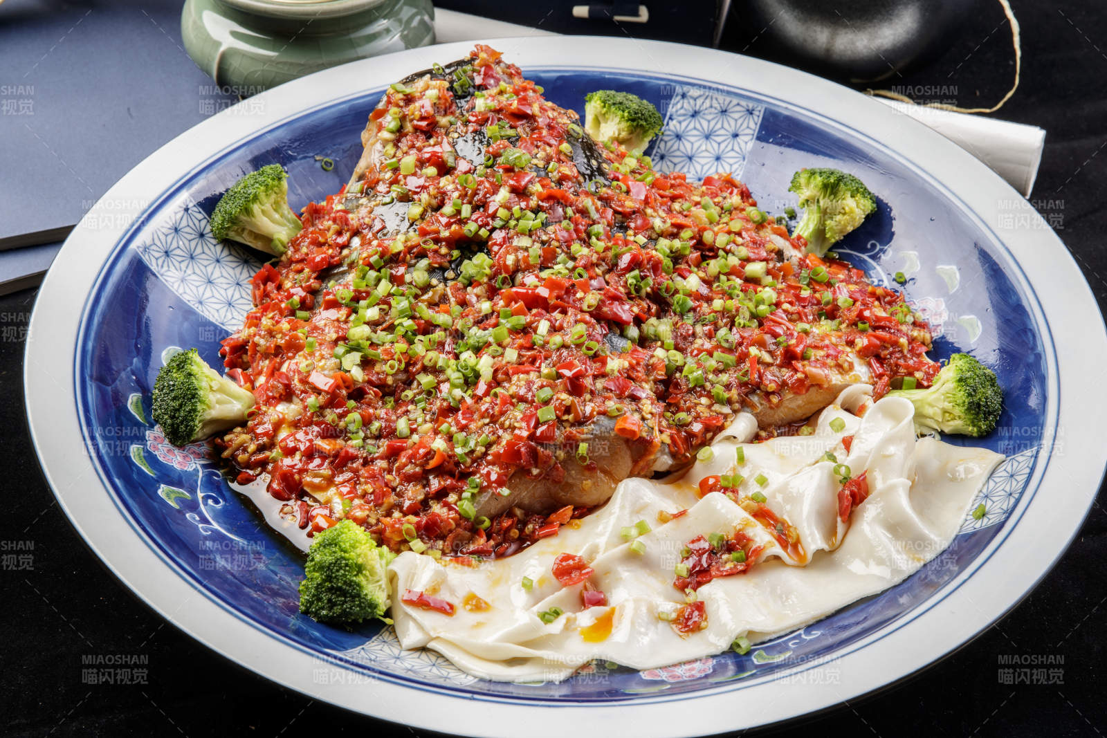 青花瓷盘装的剁椒鱼头盖面摆放在黑色背景上