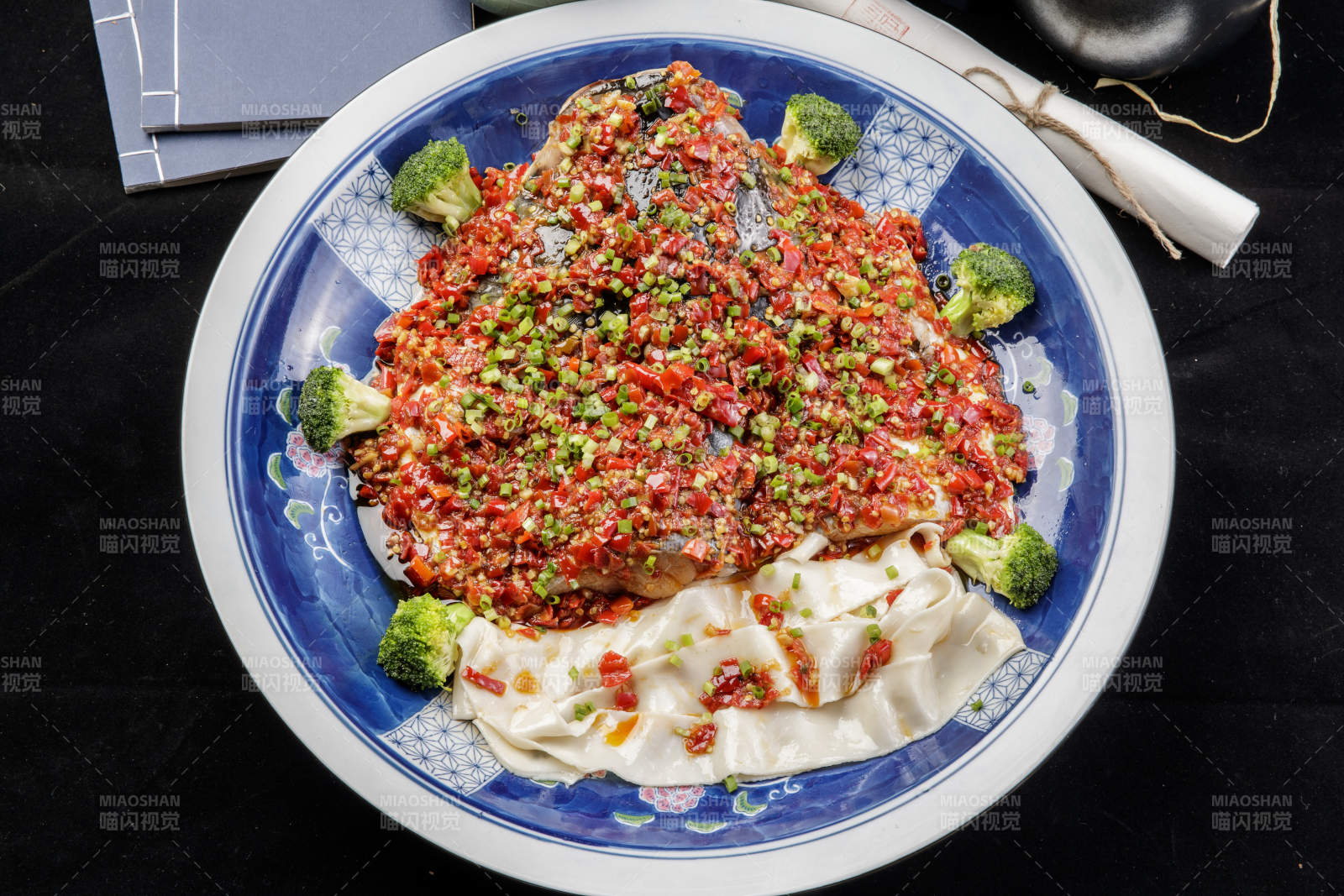 青花瓷盘装的剁椒鱼头盖面摆放在黑色背景上