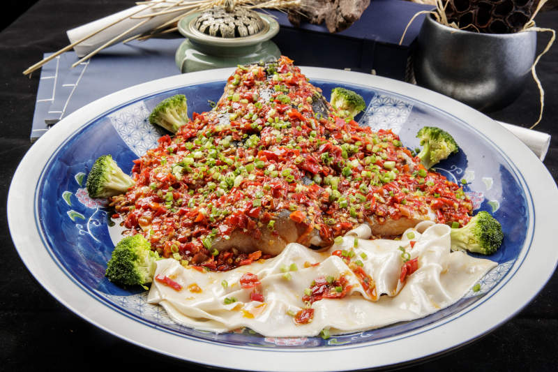 青花瓷盘装的剁椒鱼头盖面摆放在黑色背景上