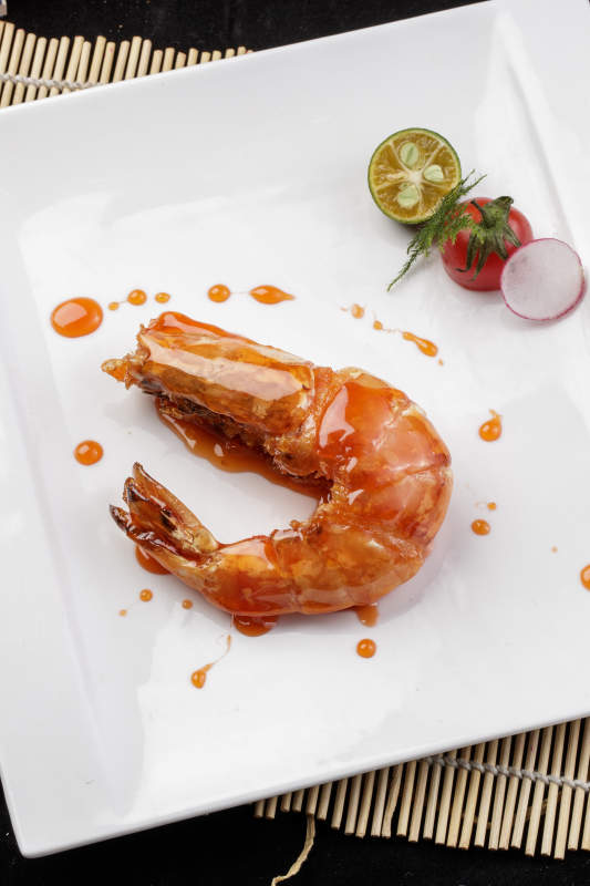 方形瓷盘装的油煎浇汁深海虾摆放在寿司帘上