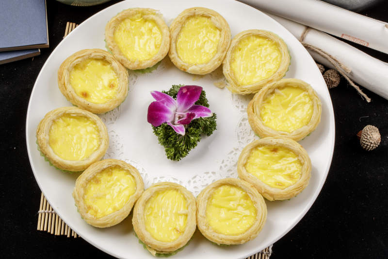 白色瓷盘装的葡式蛋挞摆放在寿司帘上