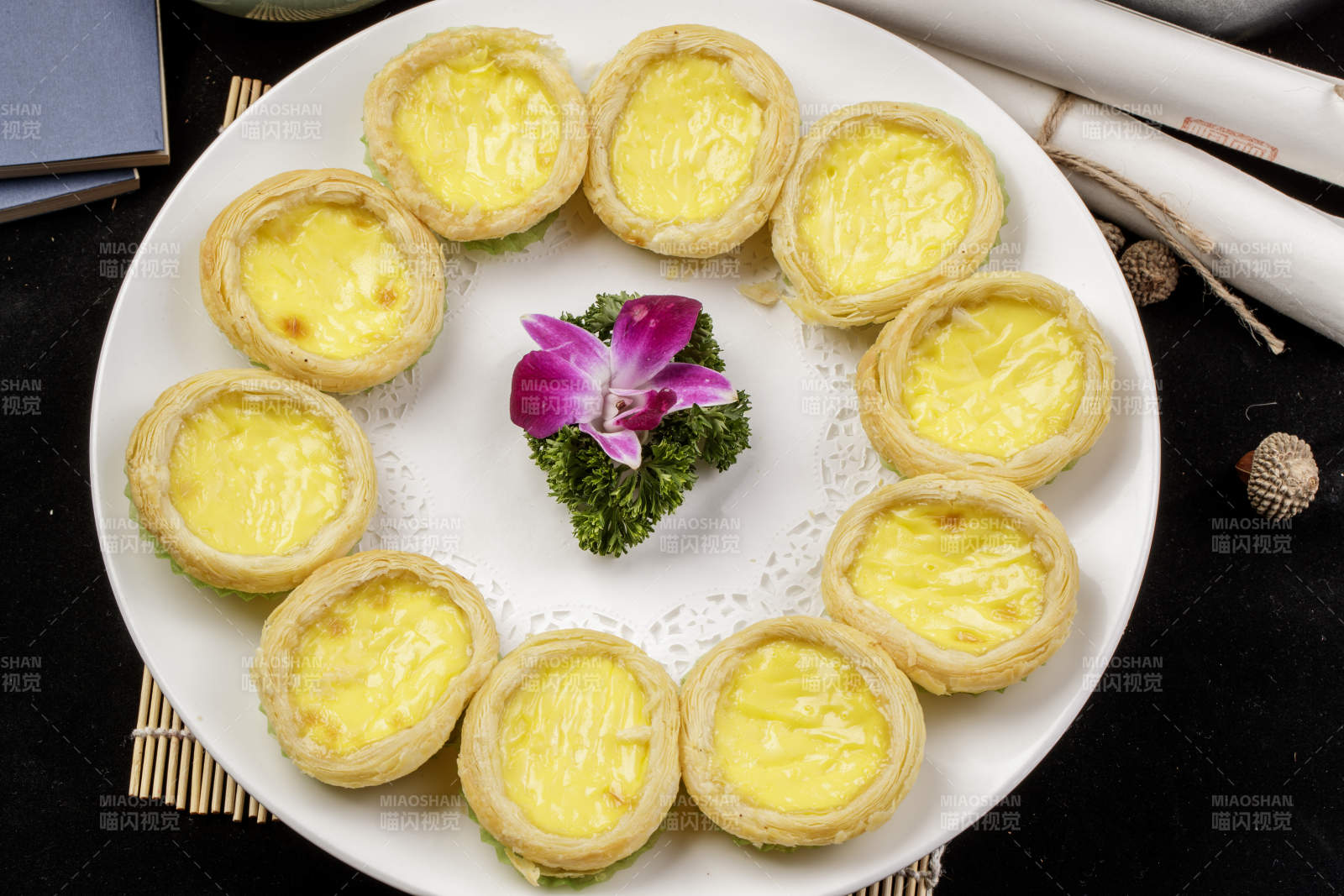 白色瓷盘装的葡式蛋挞摆放在寿司帘上