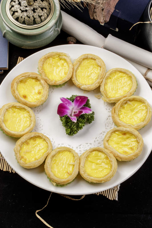 白色瓷盘装的葡式蛋挞摆放在寿司帘上