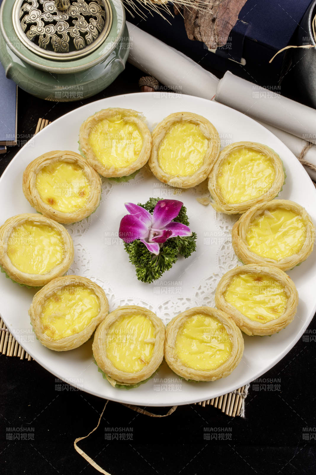 白色瓷盘装的葡式蛋挞摆放在寿司帘上