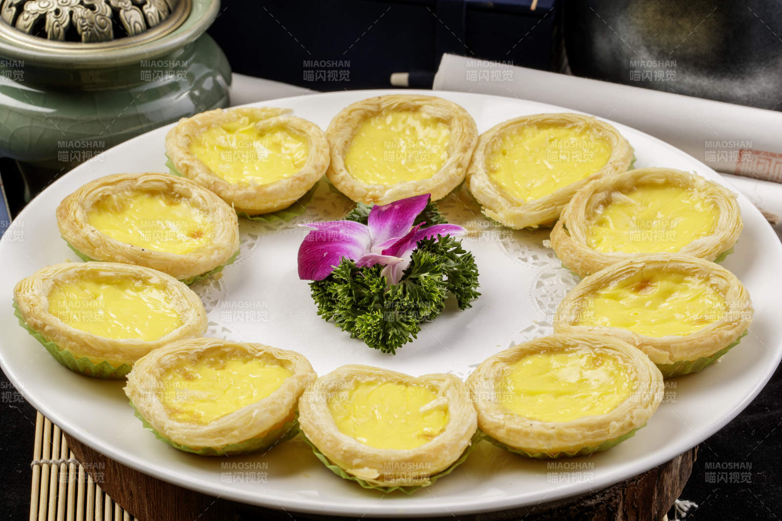 白色瓷盘装的葡式蛋挞摆放在寿司帘上