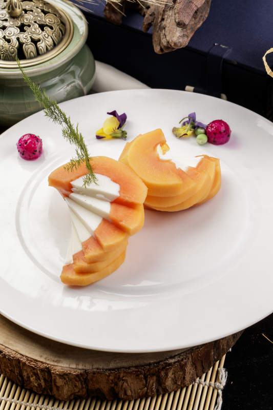 白色圆瓷盘装的木瓜蛋白摆放在樟木砧板上