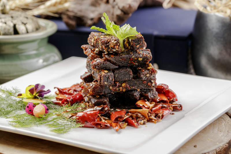 方形瓷盘装的麻辣牛肉摆放在樟木砧板上