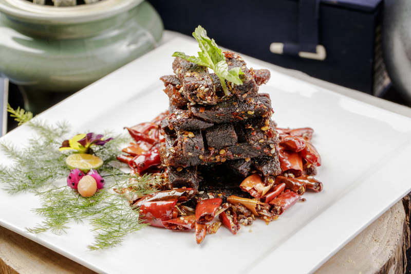 方形瓷盘装的麻辣牛肉摆放在樟木砧板上