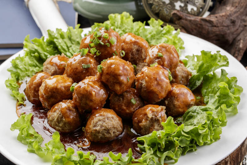 白色圆瓷盘装的红烧丸子摆放在樟木砧板上