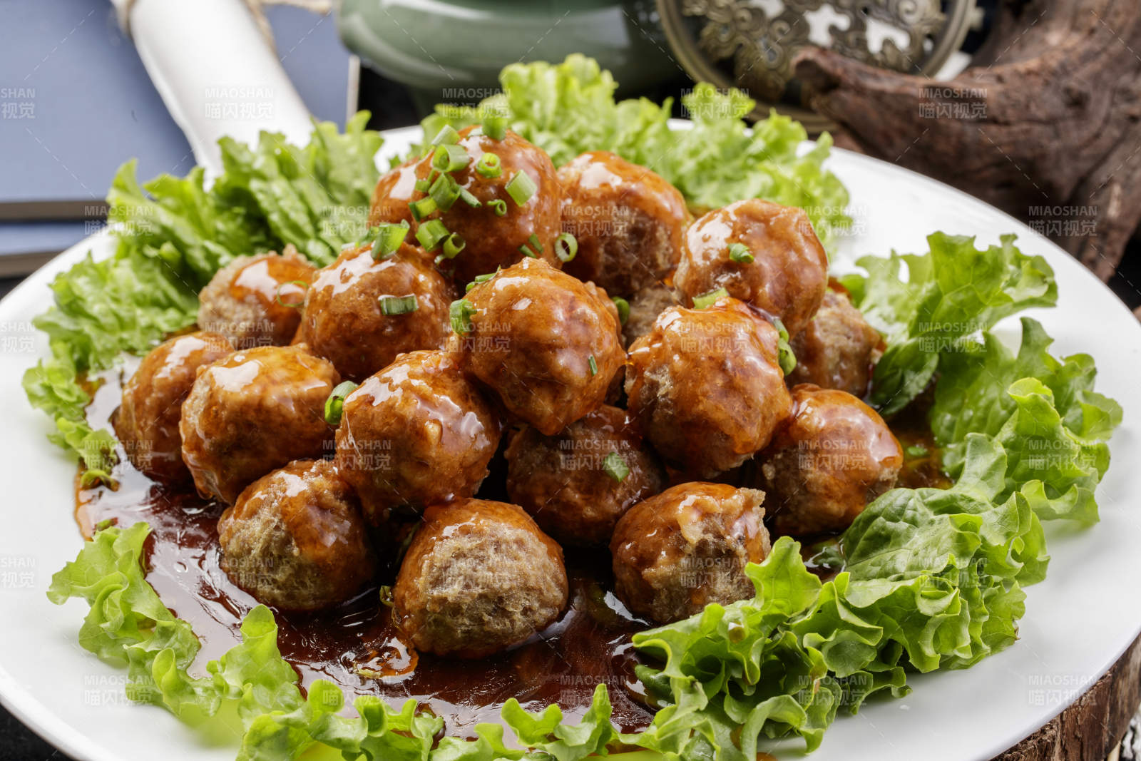 白色圆瓷盘装的红烧丸子摆放在樟木砧板上